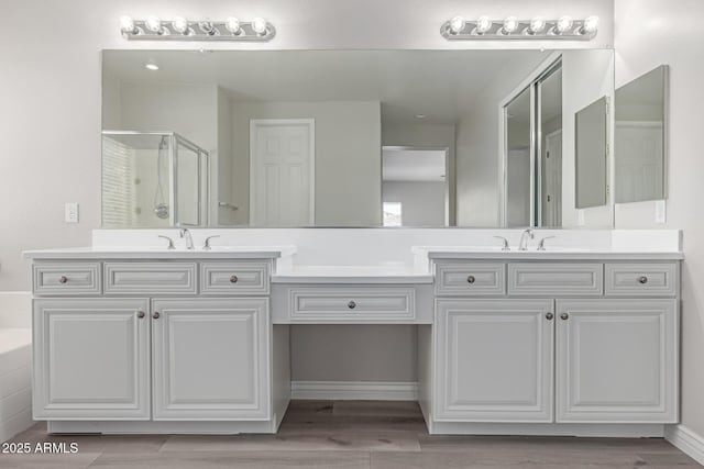 full bath featuring wood finished floors, double vanity, a sink, and a stall shower