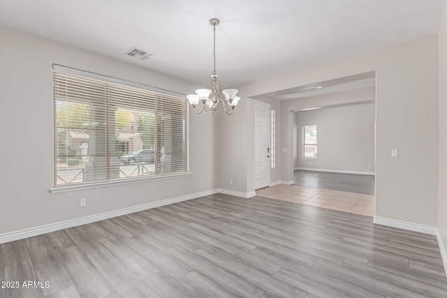 spare room with baseboards, a chandelier, wood finished floors, and visible vents