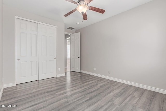 unfurnished bedroom featuring light wood-style flooring, a ceiling fan, baseboards, visible vents, and a closet