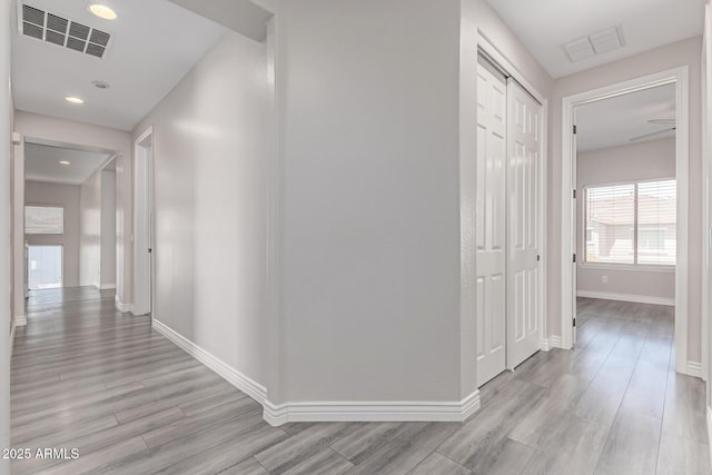 corridor with baseboards, light wood-type flooring, and visible vents