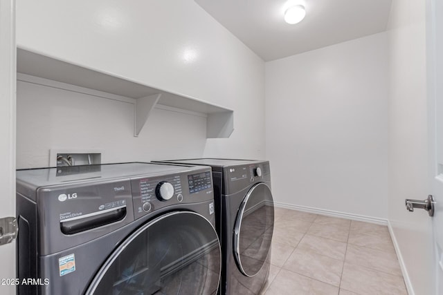 clothes washing area featuring laundry area, baseboards, light tile patterned flooring, and washing machine and clothes dryer