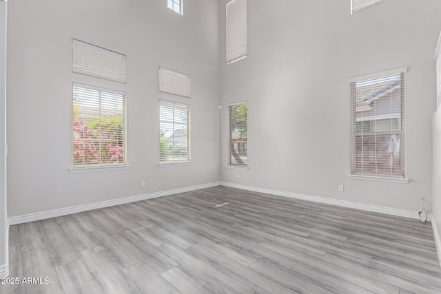 unfurnished room featuring baseboards, a high ceiling, and wood finished floors