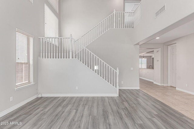 unfurnished living room with baseboards, wood finished floors, a towering ceiling, visible vents, and stairway