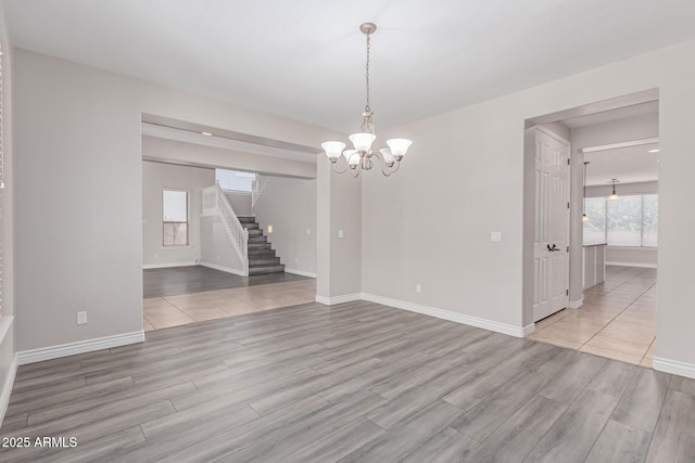 unfurnished room with baseboards, stairs, wood finished floors, and a notable chandelier