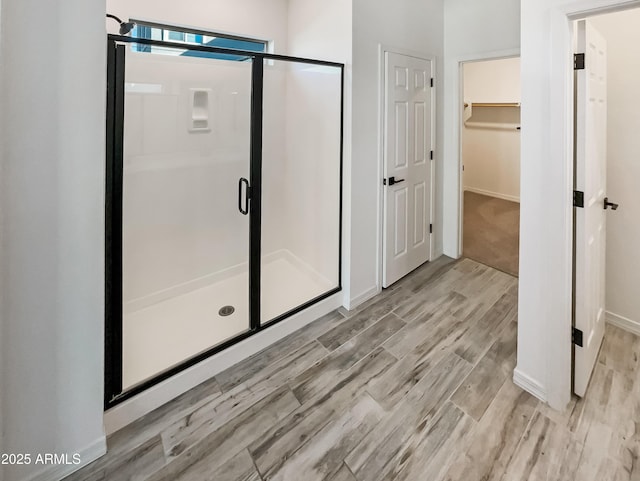 full bathroom with wood finished floors, a shower stall, a walk in closet, and baseboards