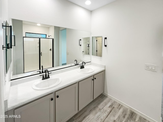 bathroom with double vanity, a stall shower, a sink, and wood finished floors