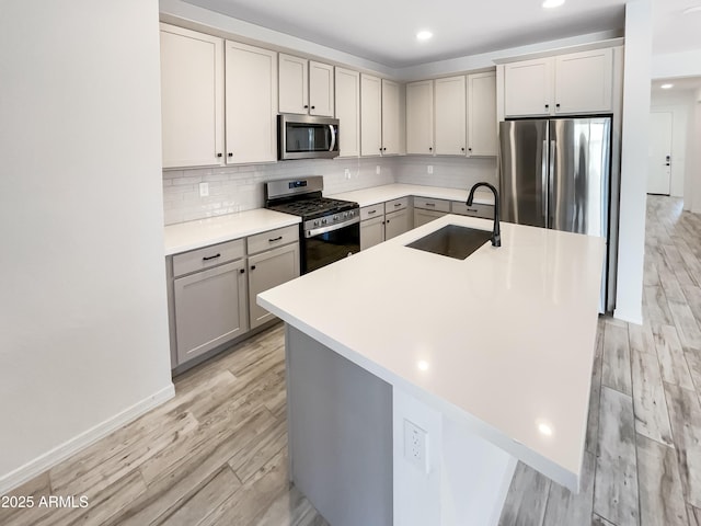 kitchen featuring stainless steel appliances, tasteful backsplash, gray cabinets, light wood-style flooring, and a sink