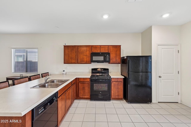 kitchen featuring a peninsula, a sink, light countertops, brown cabinets, and black appliances