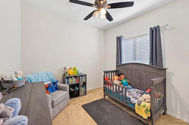 bedroom featuring a nursery area, light carpet, ceiling fan, and baseboards