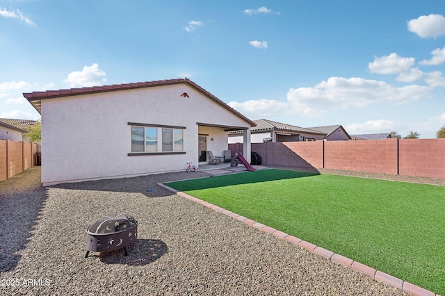 rear view of property featuring stucco siding, a lawn, an outdoor fire pit, a patio area, and a fenced backyard