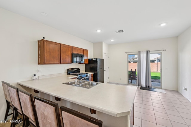 kitchen with visible vents, a peninsula, light countertops, black appliances, and a sink