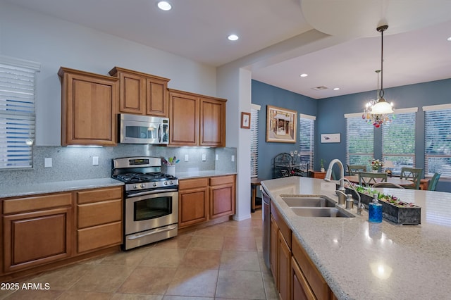 kitchen featuring light stone counters, stainless steel appliances, tasteful backsplash, hanging light fixtures, and a sink