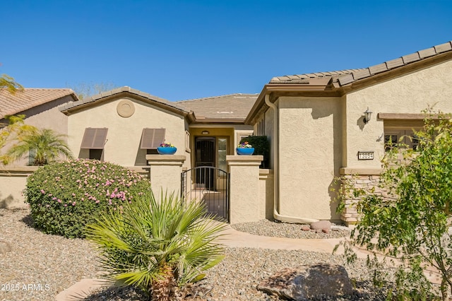 view of front facade featuring a tile roof, a gate, and stucco siding