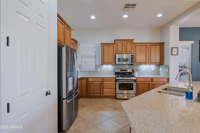 kitchen featuring light stone countertops, stainless steel appliances, a sink, visible vents, and brown cabinets