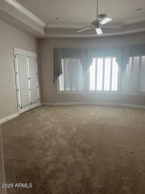 interior space featuring baseboards, a raised ceiling, a ceiling fan, ornamental molding, and carpet flooring