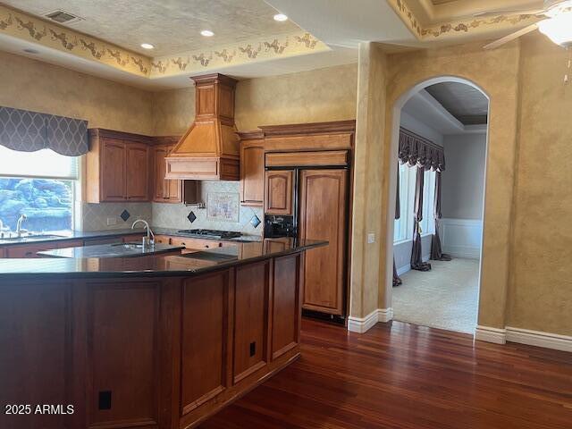 kitchen with dark countertops, a raised ceiling, custom range hood, and paneled built in refrigerator