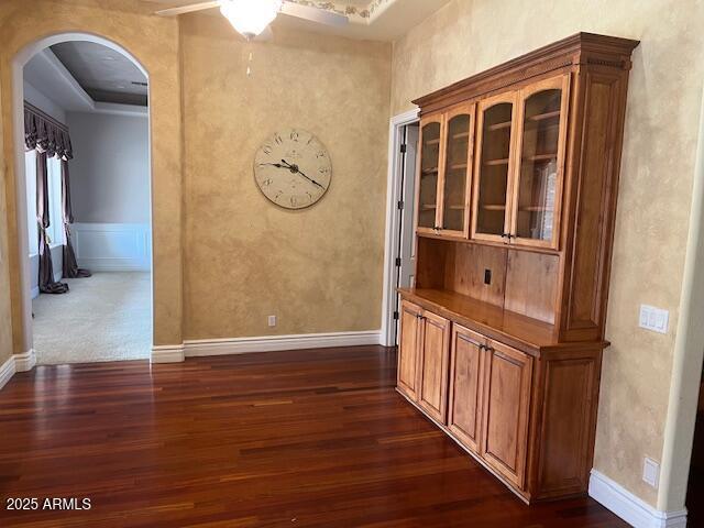 corridor featuring arched walkways, dark wood-style flooring, and baseboards