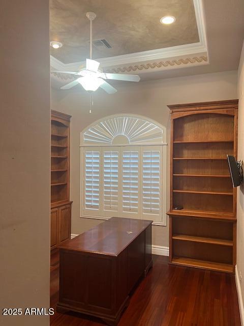 unfurnished office featuring a raised ceiling, visible vents, dark wood-type flooring, ornamental molding, and a ceiling fan