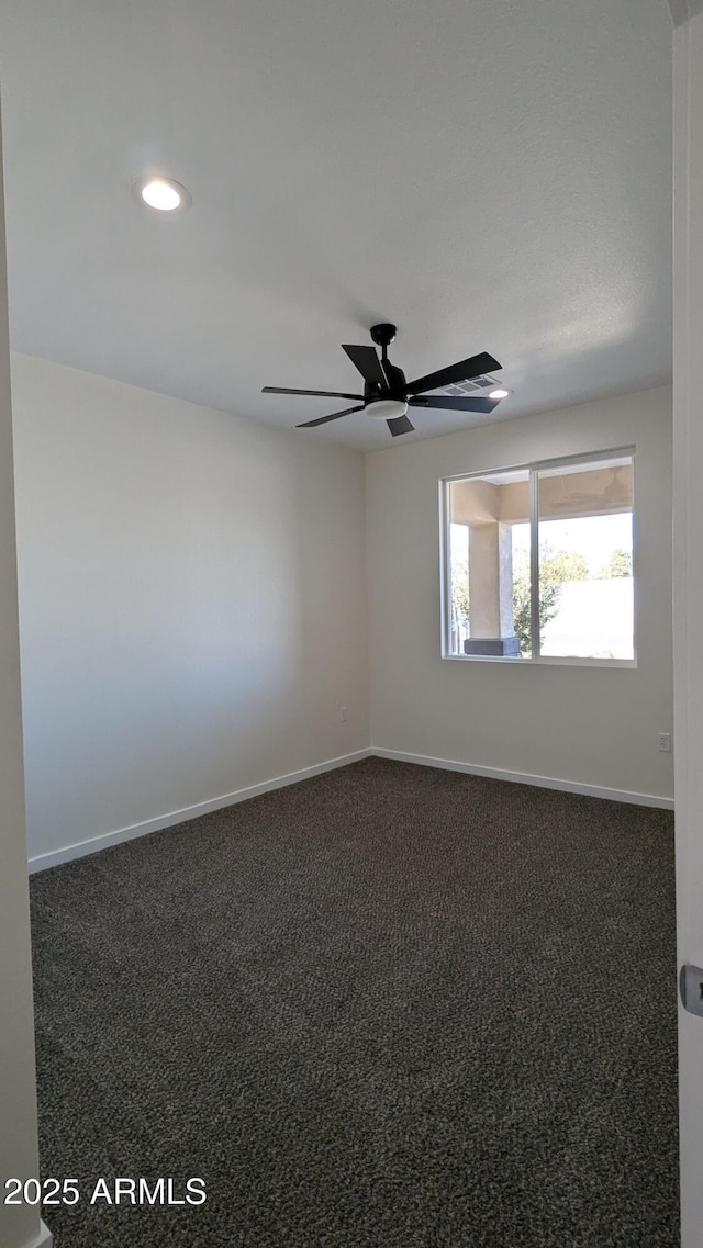 spare room with ceiling fan and dark colored carpet