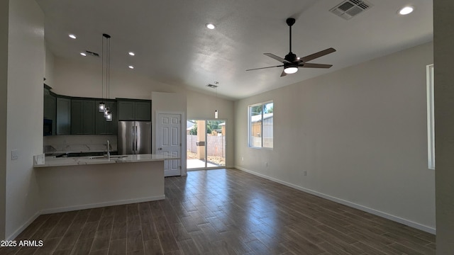 kitchen with lofted ceiling, kitchen peninsula, stainless steel refrigerator, hanging light fixtures, and light stone counters