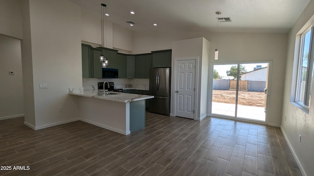 kitchen featuring a towering ceiling, sink, hanging light fixtures, kitchen peninsula, and stainless steel refrigerator