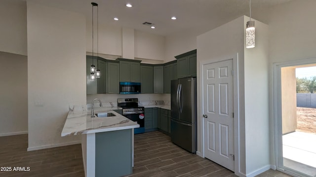 kitchen featuring kitchen peninsula, appliances with stainless steel finishes, hanging light fixtures, light stone countertops, and sink