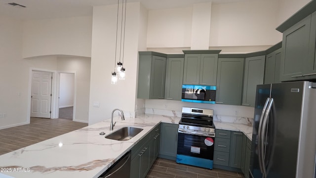 kitchen with decorative light fixtures, sink, light stone counters, and stainless steel appliances