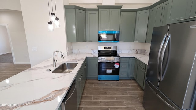 kitchen featuring stainless steel appliances, sink, hanging light fixtures, light stone counters, and green cabinets