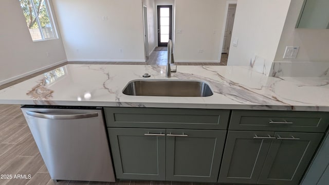 kitchen with green cabinets, dishwasher, light stone counters, and sink