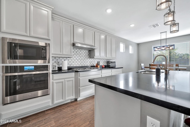 kitchen featuring dark wood-type flooring, hanging light fixtures, sink, decorative backsplash, and appliances with stainless steel finishes