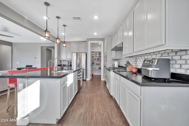 kitchen featuring dark wood-type flooring, sink, pendant lighting, white cabinets, and an island with sink