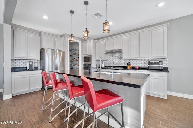 kitchen featuring appliances with stainless steel finishes, a center island with sink, tasteful backsplash, and hardwood / wood-style floors