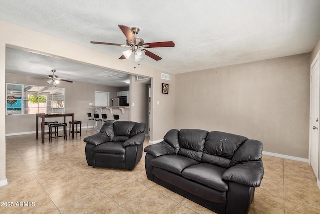 living area featuring baseboards, a textured ceiling, ceiling fan, and light tile patterned floors