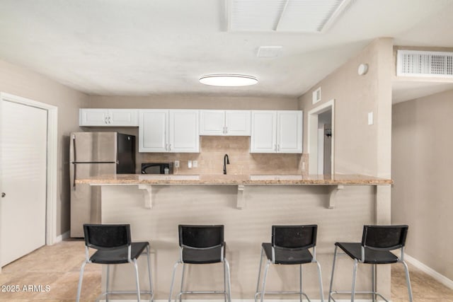 kitchen with freestanding refrigerator, a breakfast bar area, white cabinetry, and visible vents