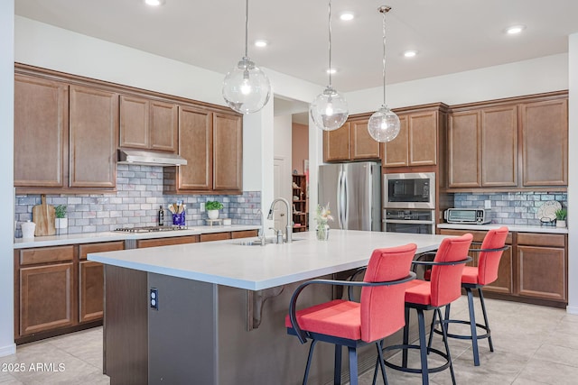 kitchen with stainless steel appliances, under cabinet range hood, a breakfast bar, a center island with sink, and a sink