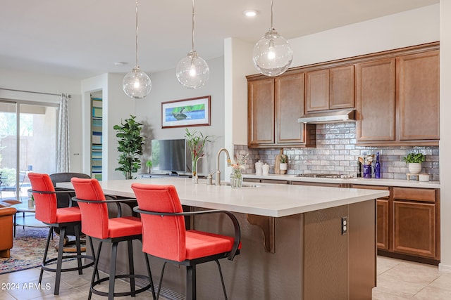 kitchen featuring sink, a breakfast bar, pendant lighting, a kitchen island with sink, and tasteful backsplash