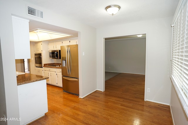 kitchen with white cabinets, stainless steel appliances, dark stone counters, and light hardwood / wood-style flooring