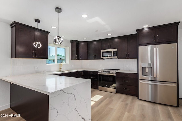 kitchen with appliances with stainless steel finishes, sink, kitchen peninsula, hanging light fixtures, and light hardwood / wood-style flooring