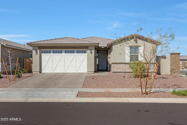 view of front facade with decorative driveway, a tile roof, an attached garage, and stucco siding