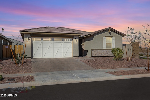 view of front of house featuring a tiled roof, decorative driveway, an attached garage, and stucco siding