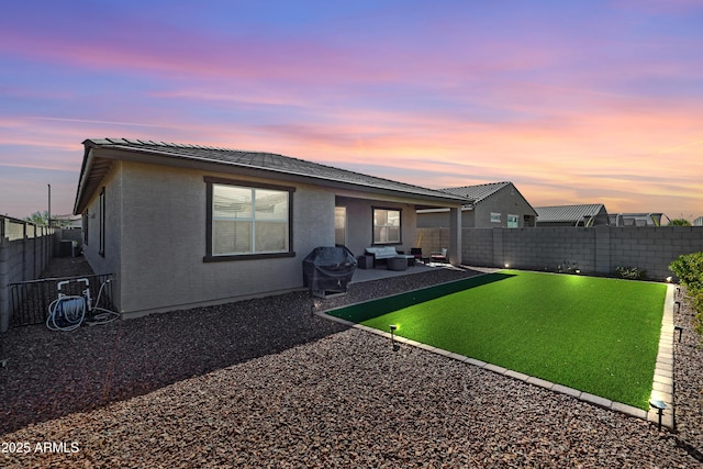 back of property at dusk with stucco siding, a patio, and a fenced backyard