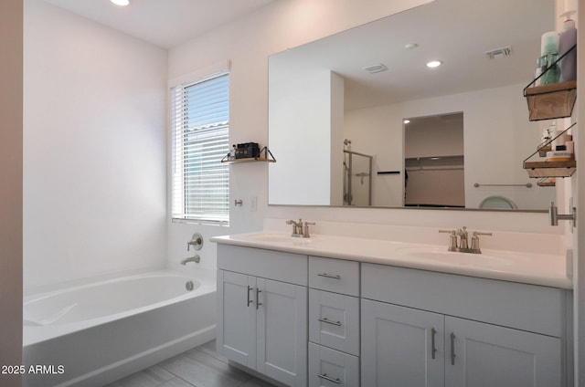 full bathroom featuring double vanity, a bath, visible vents, and a sink