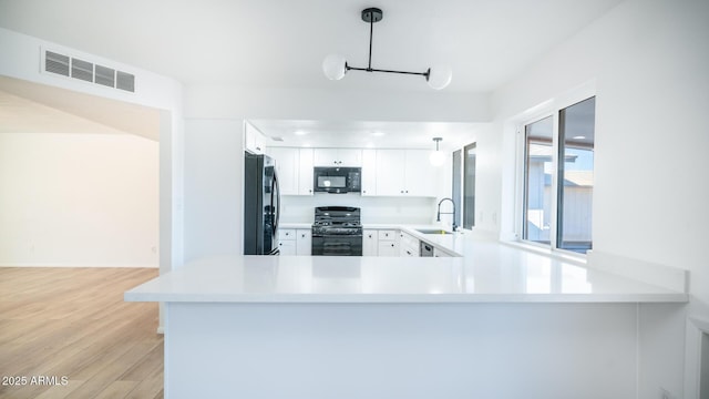 kitchen with kitchen peninsula, white cabinetry, sink, and black appliances