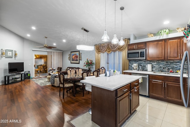 kitchen featuring ceiling fan, stainless steel appliances, decorative backsplash, hanging light fixtures, and a center island