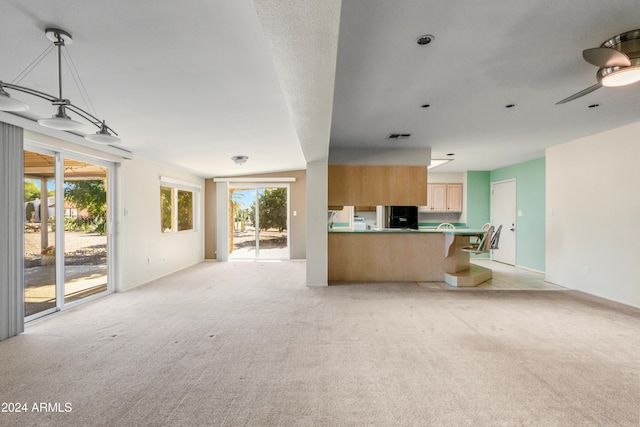 unfurnished living room featuring ceiling fan, a healthy amount of sunlight, and light carpet