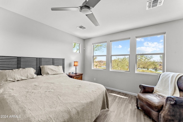 bedroom featuring light wood-type flooring, a water view, and ceiling fan