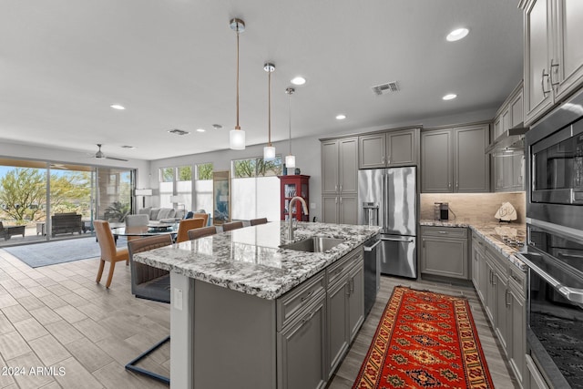 kitchen featuring gray cabinetry, stainless steel appliances, ceiling fan, a kitchen island with sink, and sink