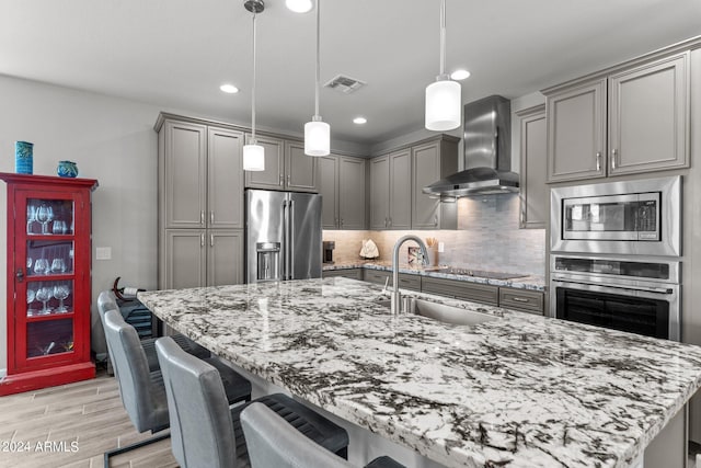 kitchen featuring appliances with stainless steel finishes, pendant lighting, sink, and wall chimney range hood