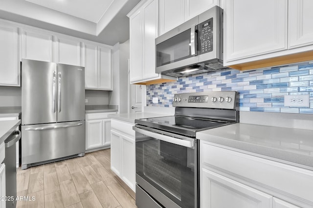 kitchen featuring tasteful backsplash, appliances with stainless steel finishes, white cabinets, and light wood-type flooring