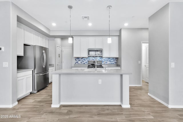 kitchen featuring pendant lighting, stainless steel appliances, an island with sink, and white cabinets